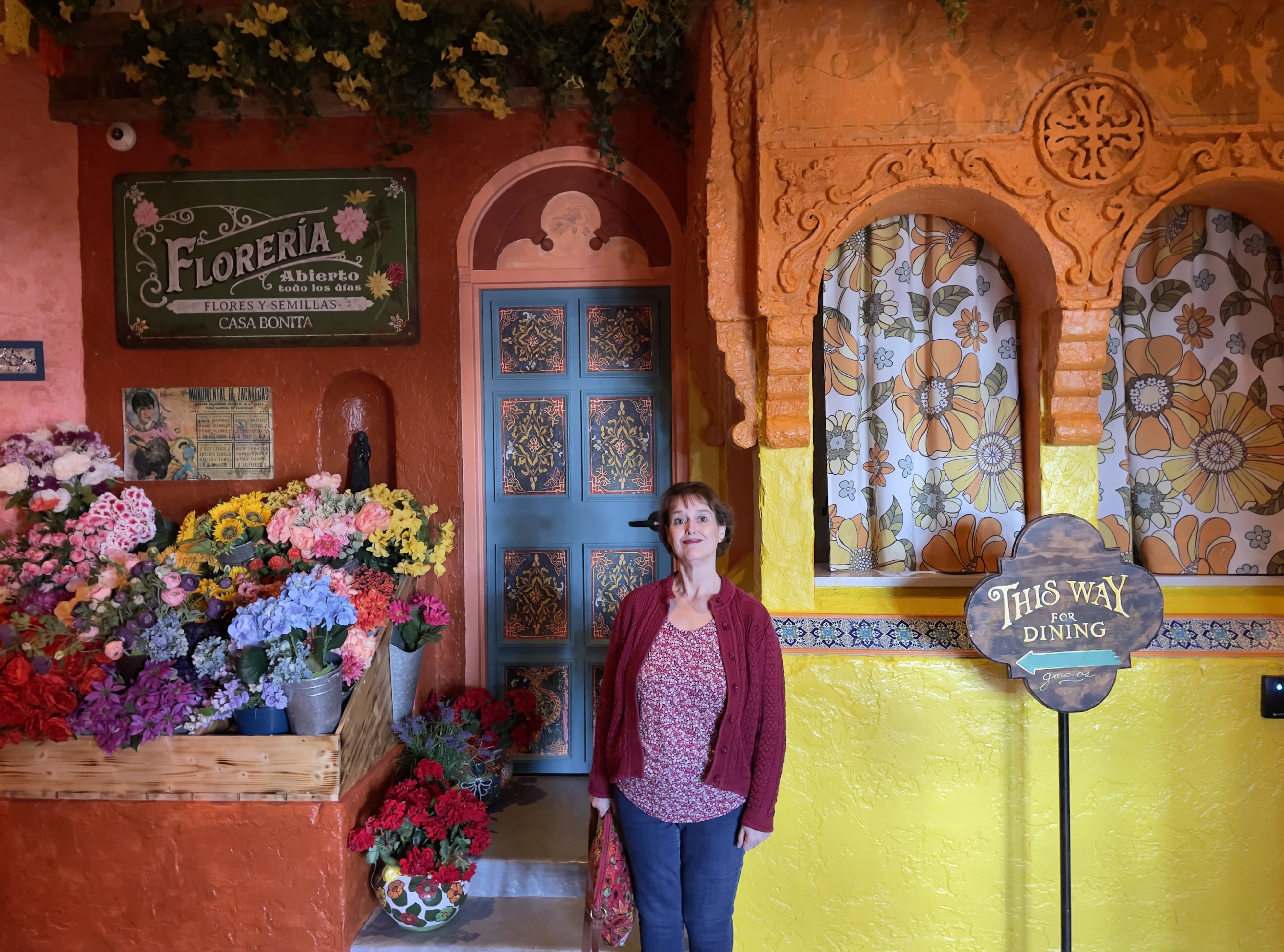 Kathy waits in line in front a colorful display of flowers and an equally colorful Mexican storefront at Casa Bonita.