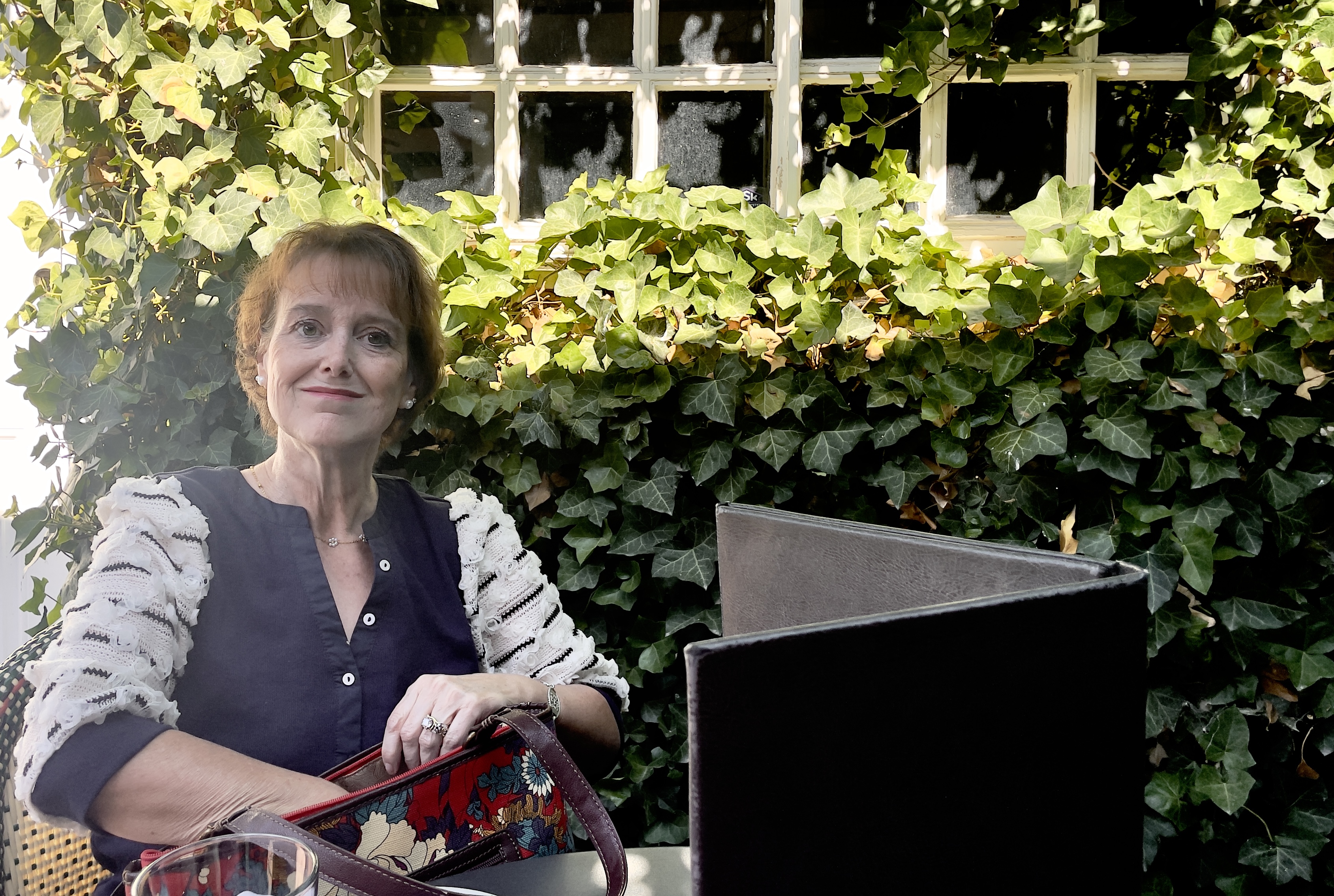 Kathy sits at the corner table of the patio, surrounded by ivy, at Finca.