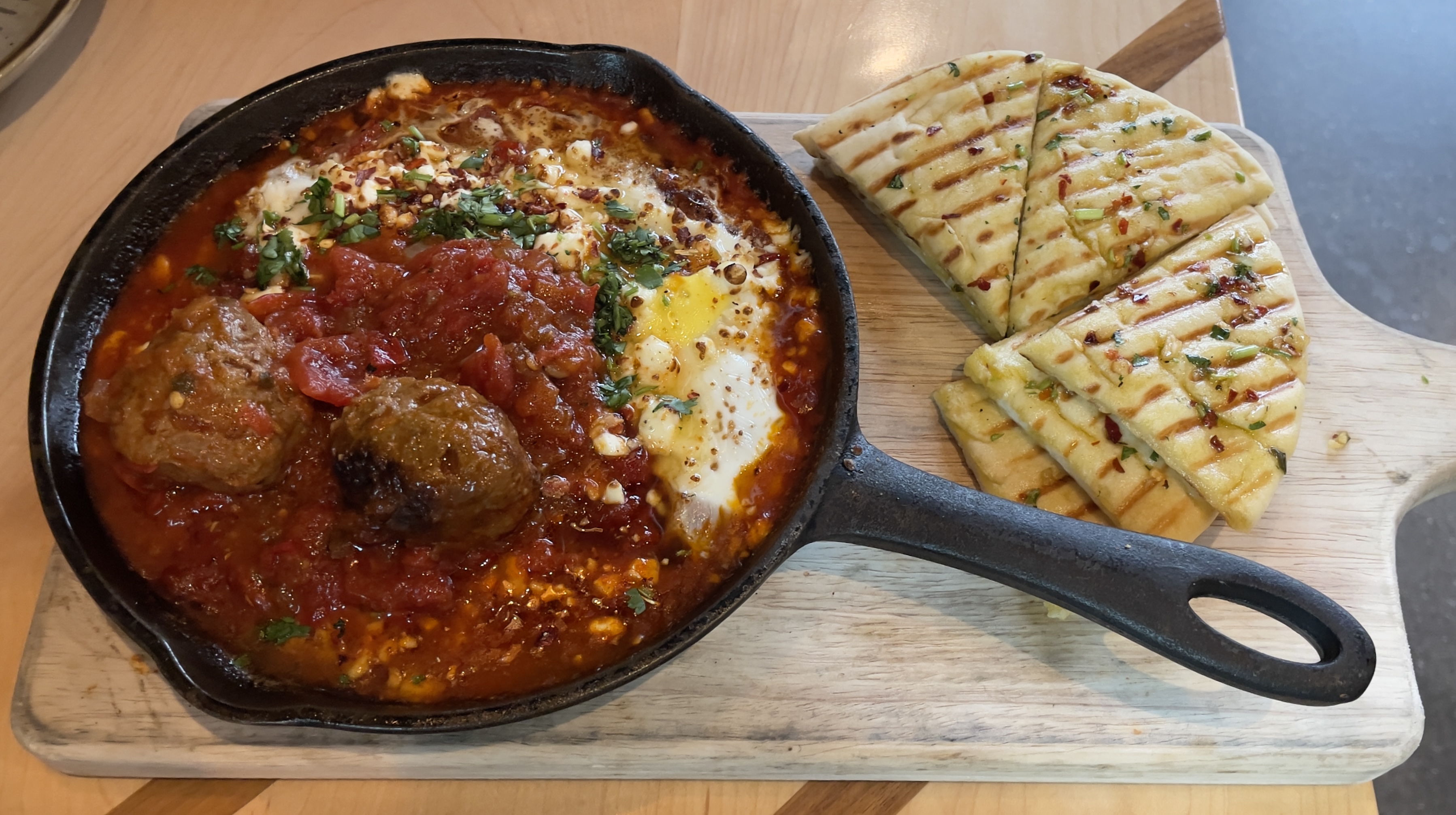 Shakshuka at Laziz Kitchen.  Soft baked eggs and lamb meatballs served in a robust tomato sauce, garnished with feta, cilantro & drizzled with honey.  Served with a side of pita Batata Harra style.